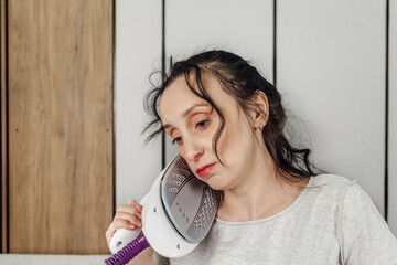 Portrait of Tired middle age woman holding an iron to her head.