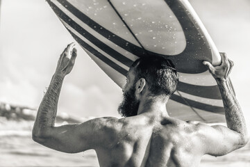 Young hipster man with surfboard on his head greeting friends with a gesture - Guy having fun doing extreme sport - Sporty bearded man training with surfboard on the sea - Black and white editing