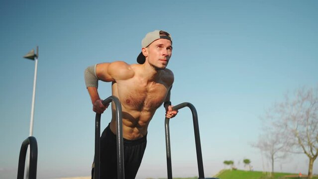 Muscular man doing push ups exercises on parallel bars. Male athlete workout outdoor gym, Strength and motivation. Medium shoot front view. Bodyweight training. Modern calisthenics park