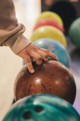 Cropped image of man's hand picking up brown bowling ball from rack