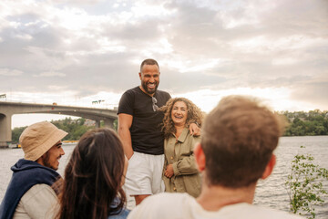 Happy couple talking to male and female friends during picnic against sky