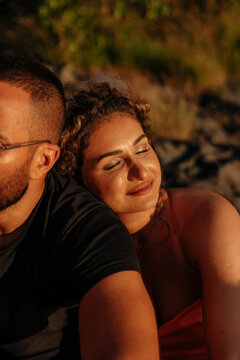 Smiling woman with eyes closed resting on boyfriend's shoulder during sunset