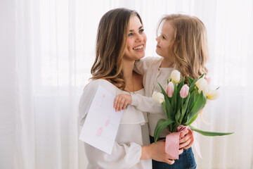 Happy mother's day. Child daughter congratulates moms and gives her a postcard and flowers tulips.