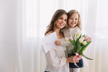 Happy mother's day. Child daughter congratulates moms and gives her a postcard and flowers tulips.