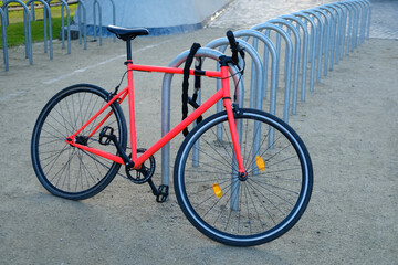 Fototapeta na wymiar bright red, scarlet classic bicycle in urban landscape sunset parked in bike parking lot, punctured wheel problem, repair of vehicles in city, public bike rental, bike saddle sharing, property theft