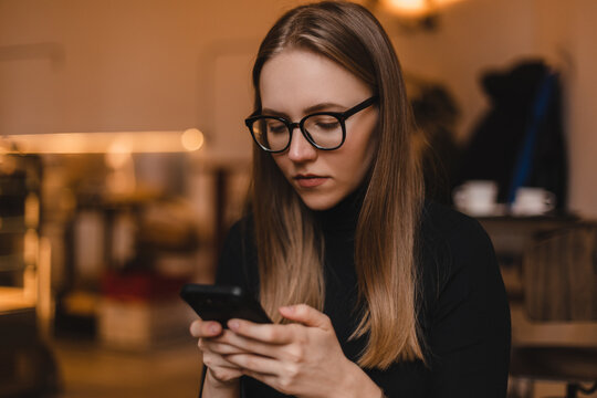 Charming woman with beautiful smile reading good news on mobile phone during rest in coffee shop, happy Caucasian female watching her photos on cell telephone while relaxing in cafe during free time.
