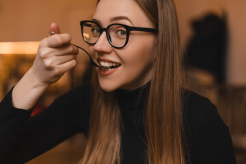 Pretty young woman enjoying cake while sitting in cafe. Woman wear black eye glasses and long sleeves top. She look enjoy, smiling and happy. Delicious lunch in cafe.