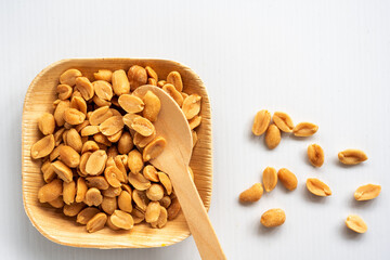 Roasted unsalted peanuts, are served in a biodegradable palm leaf tray and a spoon on a white background.