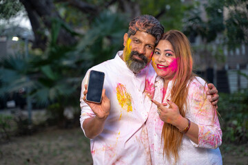 Fototapeta premium young indian couple looking at smartphone and playing holi