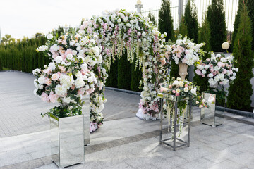 Wedding ceremony outdoor. A beautiful and stylish wedding arch, decorated by various fresh white flowers, standing in the garden. Celebration day.