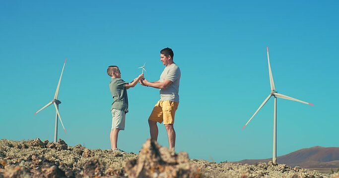 Happy father and son on looking at wind energy turbine sat wind farm site, alternative energy, wind farm and happy time with your family.
