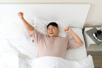 Happy asian man enjoying good morning, stretching in bed