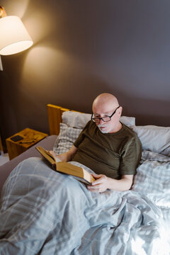 Senior man wearing eyeglasses while reading book on bed at home