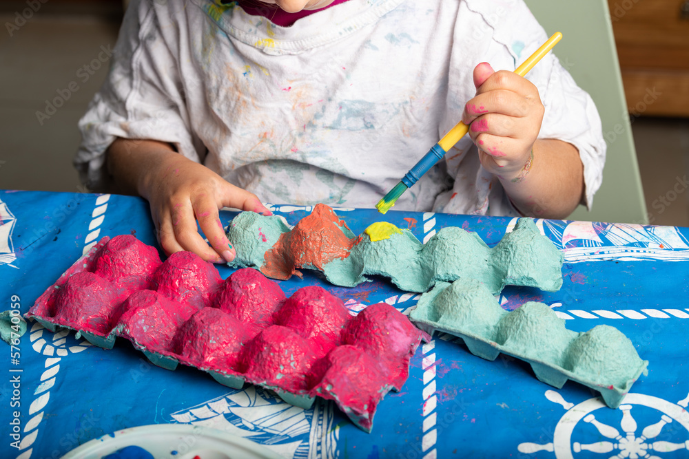 Wall mural child painting an egg box with a brush