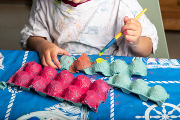 Child painting an egg box with a brush - 576740059