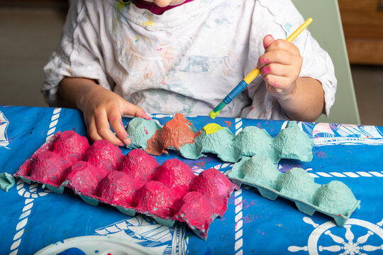 Child painting an egg box with a brush