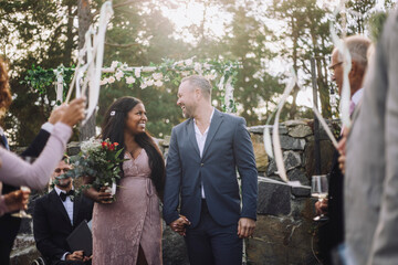 Cheerful newlywed couple holding hands while walking amidst guests at wedding ceremony