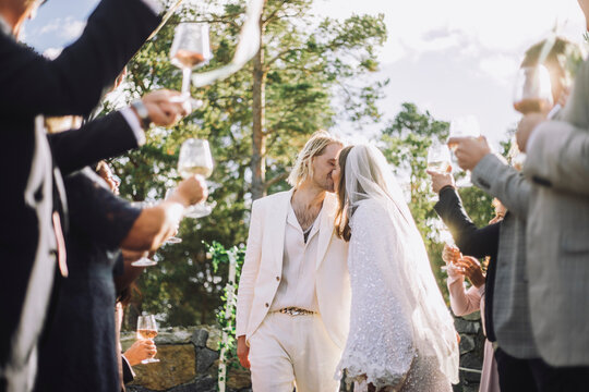 Affectionate bride and groom kissing on mouth amidst guests raising toasts at wedding ceremony