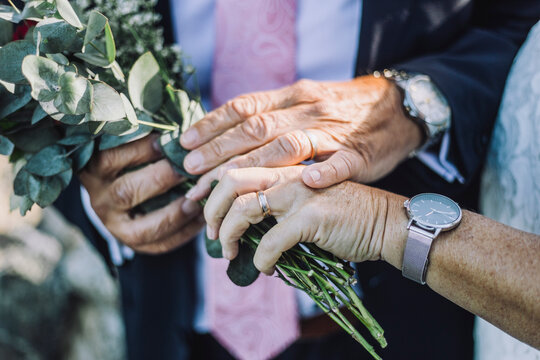 Cropped image of newlywed couple showing rings while holding bouquet during wedding ceremony