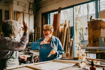 Happy senior craftswomen giving high-five at carpentry workshop