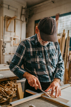Senior craftsman scraping frame with chisel while working at carpentry workshop