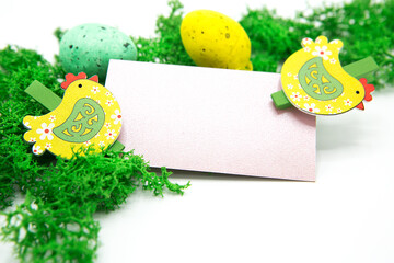 Blank greeting card with wooden decorative clothespins in the shape of chickens and painted eggs on moss. Birthday, spring and easter concept.