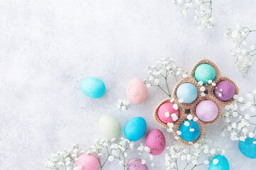 Easter holiday greeting card. Top view photo of colorful Easter eggs in knitted basket and white gypsophila flowers on stone table.