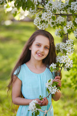 Portrait of a young girl in a blooming apple orchard. A young girl with loose long hair. Spring portrait of a beautiful girl in a blooming garden. Vertical orientation