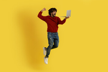 Emotional indian man jumping in the air with laptop