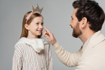 happy bearded man touching nose of cute daughter in crown isolated on grey.