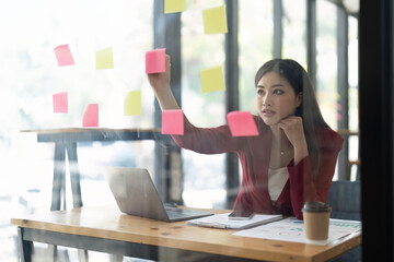 A woman using a sticky note and analysis data report during writing make note some data on notepad, Business financial concept