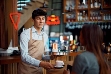 Young waiter serving coffee to customer in cafe.