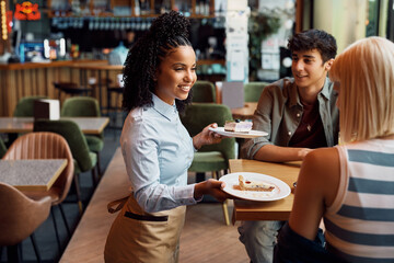 Happy black waitress serving dessert to couple in cafe. - obrazy, fototapety, plakaty