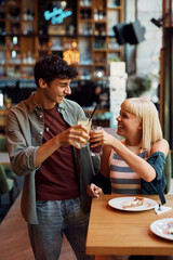Young cheerful couple toasting while eating cake in cafe.