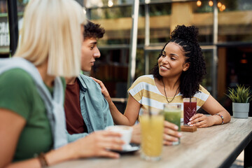 Happy African American woman communicating with her friends while drinking juice in cafe.