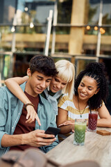 Young happy friends surfing the net on smart phone in cafe.