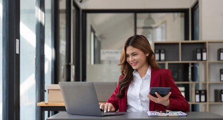 Asian Business woman using calculator and laptop for doing math finance on an office desk, tax, report, accounting, statistics, and analytical research concept