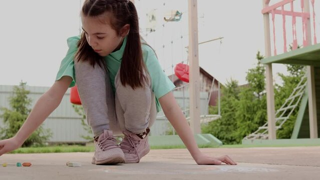 Girl draws with colorful crayons on pavement. Children's drawings with chalk on wall. Creative kid. Joy of childhood. High quality 4k footage