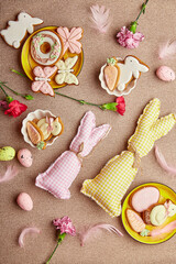 Fototapeta na wymiar Aesthetic spring Easter background flat lay. Glazing Easter cookies, handmade bunny toys, pink flowers with feathers.