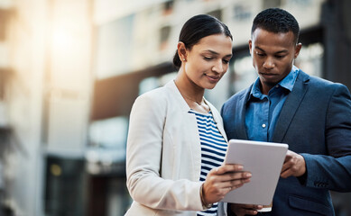 Business moves along as they do. Shot of two businesspeople using a digital tablet in the city.