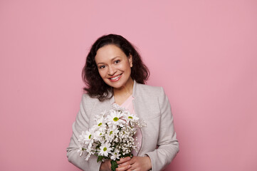 Stunning middle-aged Latin American pretty woman feeling happiness while getting cute bouquet of chrysanthemums flowers for International Women's Day, smiling at camera over isolated pink background