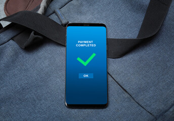 payment completed notification in a mobile phone screen, phone alongside with bag on table