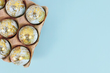 Painted Easter eggs with golden spots in egg carton on blue background with copy space