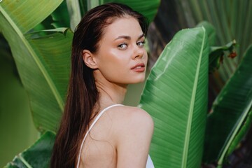 Beauty portrait of a young woman brunette with long hair in front of palm trees, face and body skin care concept, the tropics, advertising beauty products