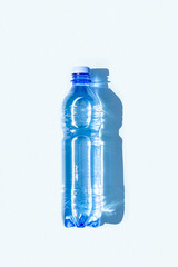 Bottled water. A bottle of mineral water with hard shadows on blue background. Flat lay Top view Copy space