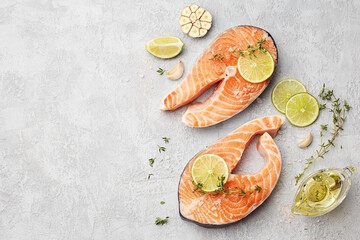 Two fresh raw salmon steaks with lime, thyme, olive oil and garlic on gray concrete background. Top...