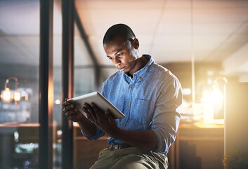In make things happen mode. Shot of a young businessman using a digital tablet during a late night...