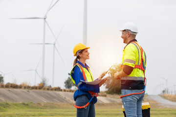 Male and female engineer wearing uniform and helmet discuss while survey the land area at wind...