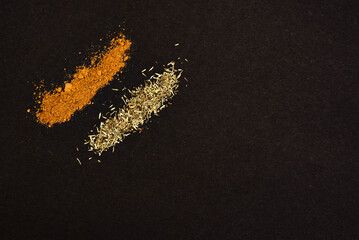 Spices scattered on a black background. Coriander and rosemary heaped on a dark background.