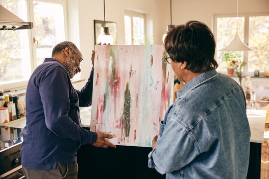 Senior couple helping each other while holding painting at home